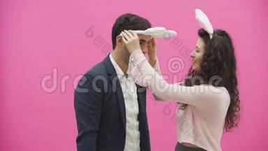 年轻情侣的粉色背景。 头上戴着黑黑的耳朵。 在这期间，女孩戴着兔子耳朵